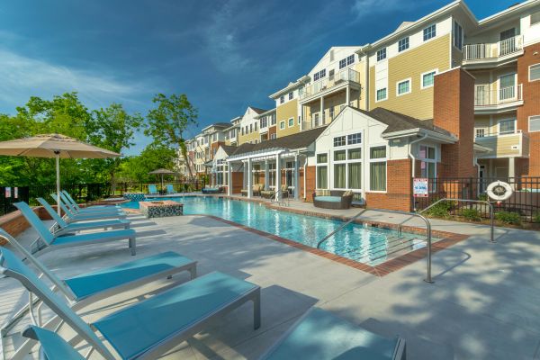 Modern apartment complex with outdoor pool, lounge chairs, and umbrellas on a sunny day.