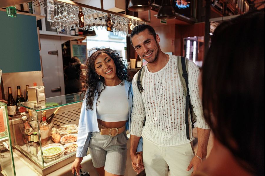 Attain on 5th apartment homes with A smiling couple holds hands in a market, standing by a counter with food dishes on display.