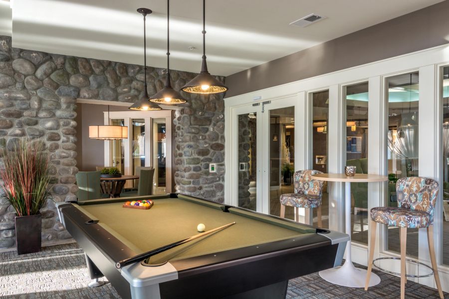 Modern game room with a pool table, stone walls, pendant lights, and bar seating near large windows.