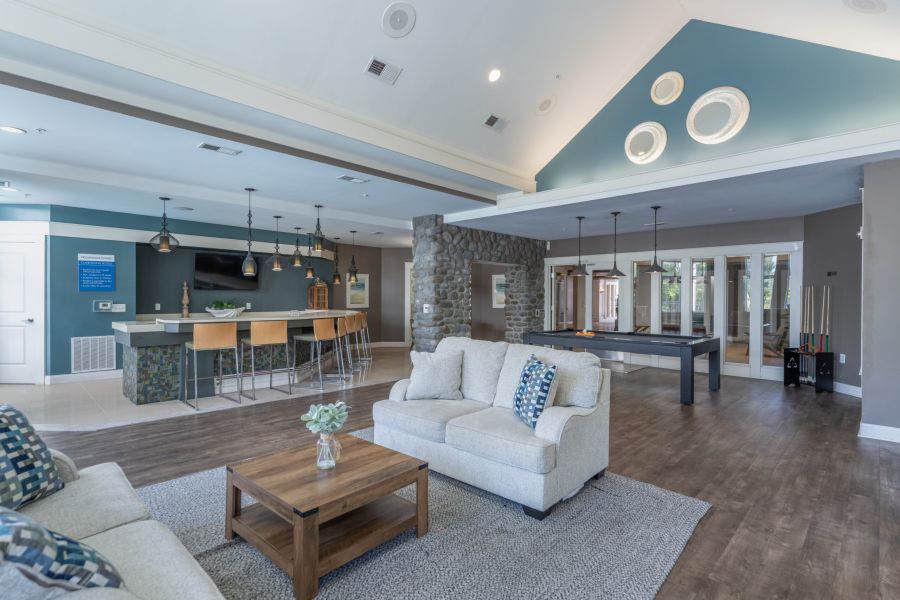 Modern lounge with sofas, a pool table, bar seating, TV, and stone accent wall, featuring wood flooring and blue-green accents.