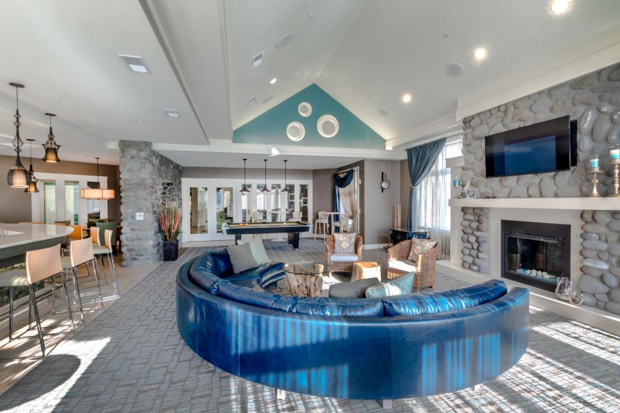 Modern lounge with a blue curved sofa, stone fireplace, TV, pool table, and large windows letting in natural light.