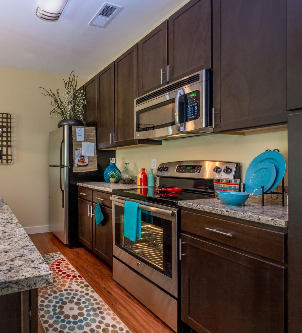 Modern kitchen with dark cabinets, granite countertops, stainless steel appliances, and teal accents.