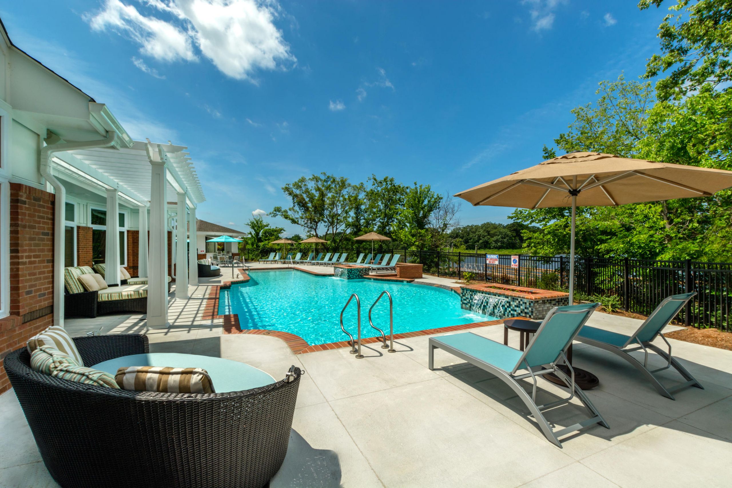 Outdoor pool area with lounge chairs, umbrellas, and clear blue sky on a sunny day.