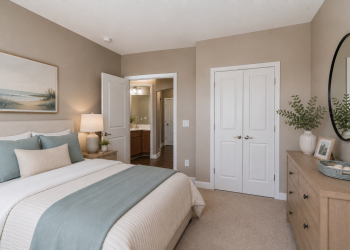 A cozy bedroom with beige walls, a bed with blue bedding, dresser, mirror, and two white doors.