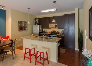 Modern kitchen with dark cabinets, granite island, red stools, and adjacent dining area with round table.