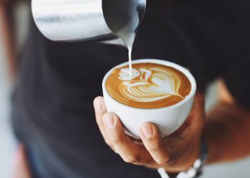 Attain on 5th apartment homes with Hand holding a cup of coffee with latte art as milk is being poured into it.
