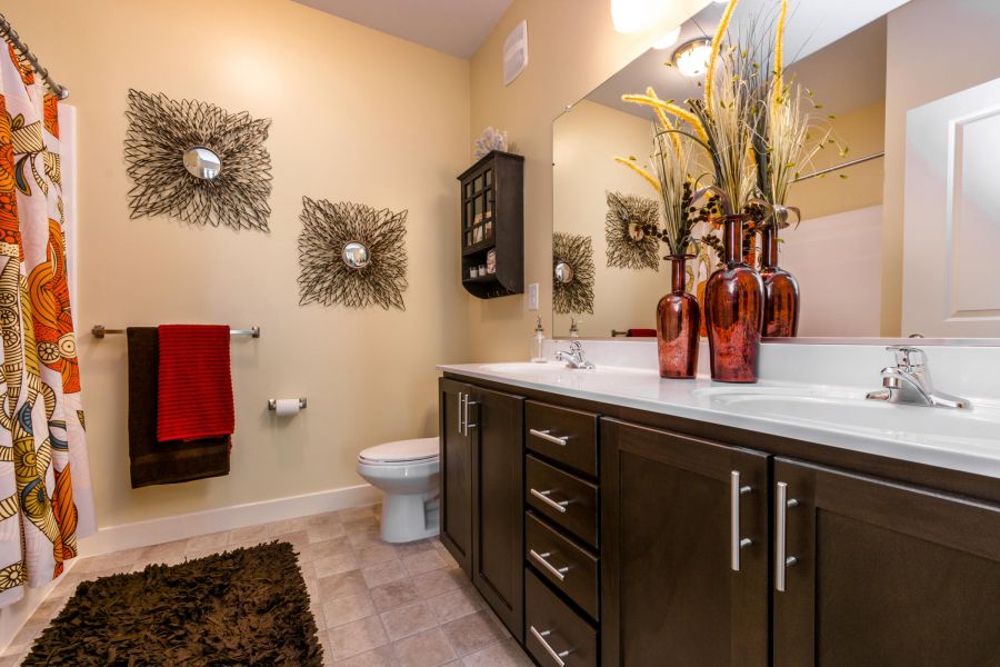 Modern bathroom with dark wood cabinets, decorative wall art, and red accents, including vases and towels.