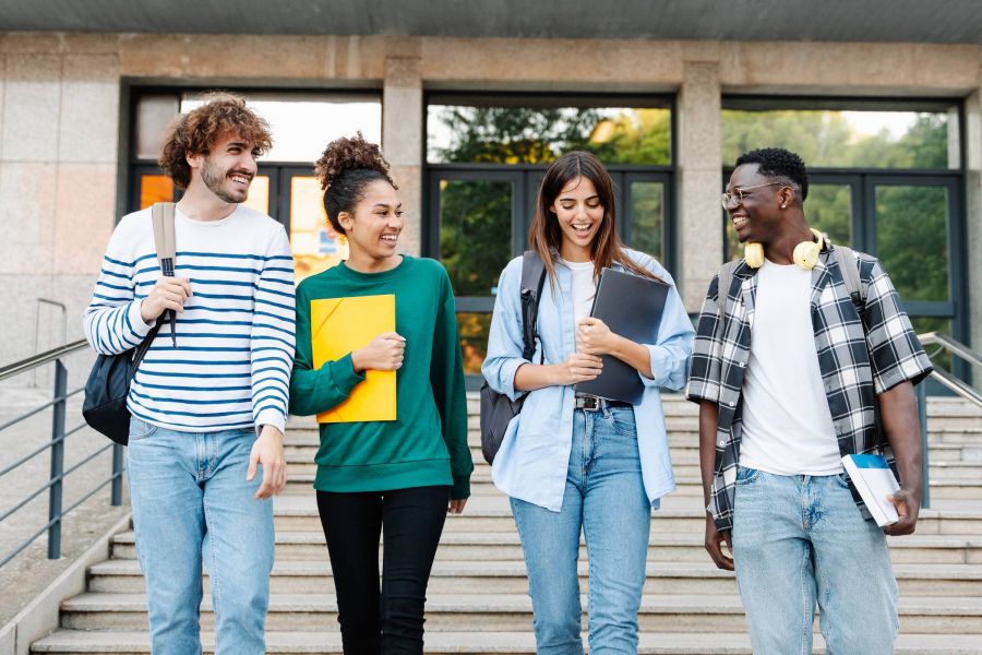 Attain on 5th apartment homes with Four smiling students walking down steps outside a building, holding books and backpacks.