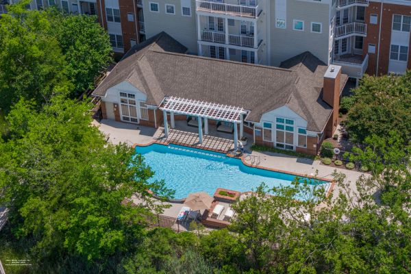 Aerial view of an apartment clubhouse with a swimming pool, surrounded by trees and lounge chairs.