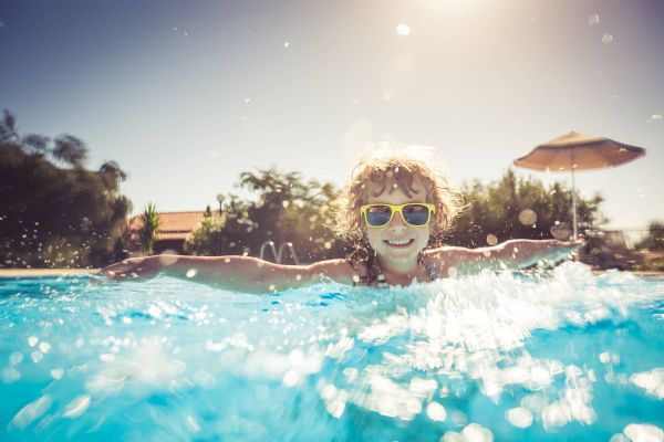 Attain on 5th apartment homes with Smiling child wearing sunglasses splashes and swims in a bright outdoor pool on a sunny day.