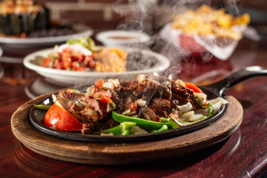Attain on 5th apartment homes with Steaming hot fajitas with beef, peppers, and onions served on a sizzling skillet on a wooden platter.