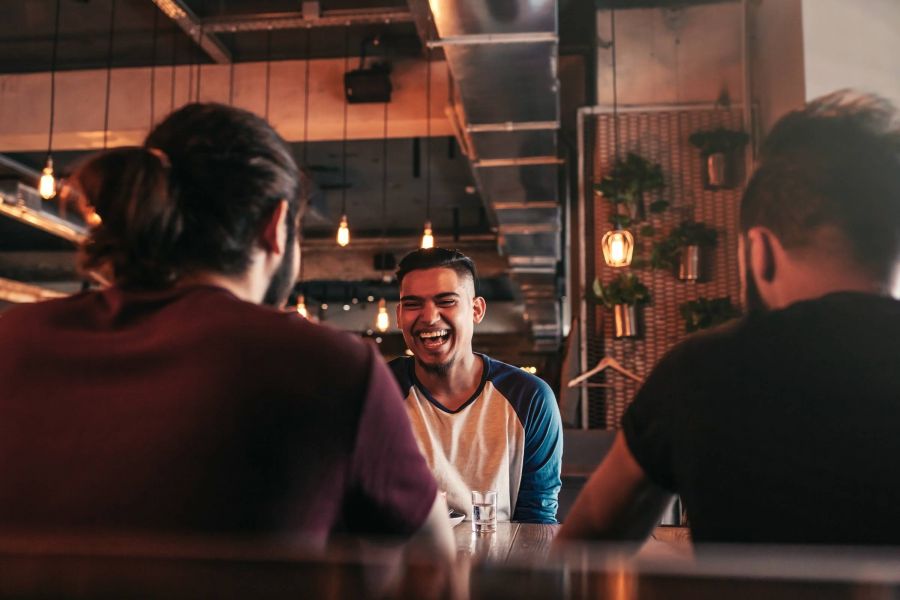 Attain on 5th apartment homes with Three young men sit at a table in a stylish cafe, with one man laughing joyfully at the center.
