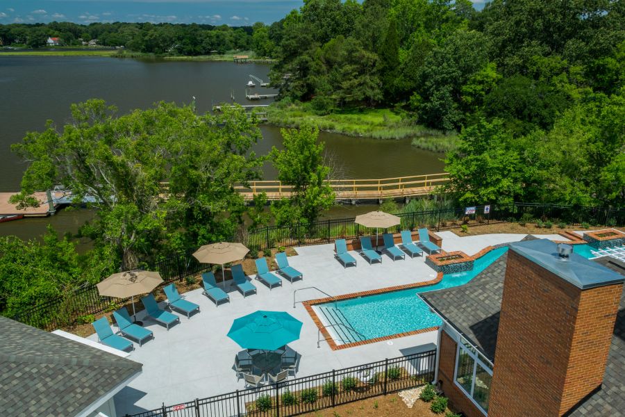 A swimming pool with lounge chairs and umbrellas overlooks a lake surrounded by trees and greenery.