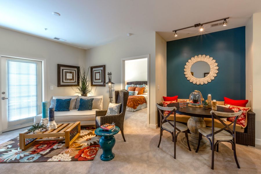 A colorful living and dining area with modern decor, a white sofa, and a round table beside a teal accent wall.