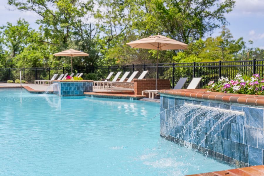 Outdoor swimming pool with waterfalls, lounge chairs, umbrellas, and surrounding greenery on a sunny day.