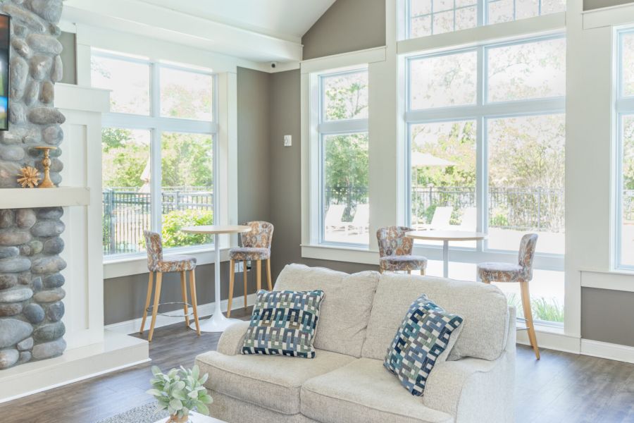 Bright living room with a beige sofa, wooden coffee table, and large windows letting in natural light, with two small dining tables.